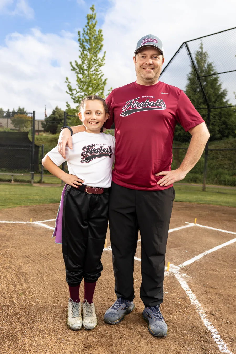 Assistant coach Ian Swanson with his daughter at home plate, both in Fireballs gear.